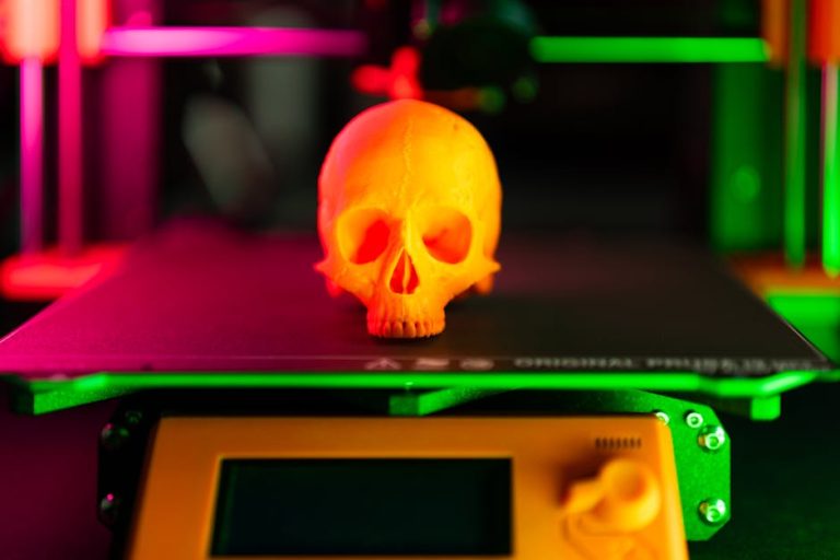Close-up of an orange 3D-printed skull on a 3D printer with vibrant lighting.